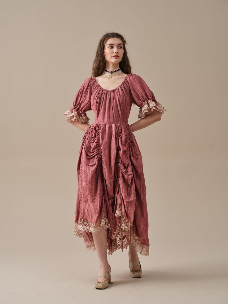 a fulllength studio shot of a young woman in a mauve midi dress.  the dress is a dusty rose color with a gathered skirt and lace detailing on the sleeves and hem. the dress has short puff sleeves and an empire waistline. the woman is wearing a delicate choker necklace and nude heels. she is posing against a plain light beige backdrop. the overall style is romantic and vintageinspired.
