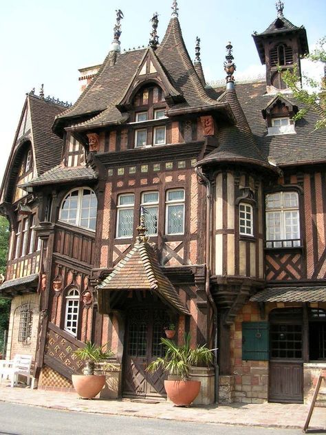 the image showcases an elaborate and picturesque halftimbered house. the house boasts multiple stories, adorned with intricate woodwork, gables, and a combination of brick and halftimbered construction. the rich brown tones of the wood contrast beautifully with the lighter brickwork. lush greenery in terracotta pots adds a touch of vibrancy to the entrance. the sunny weather casts soft shadows, enhancing the architectural details of the house.