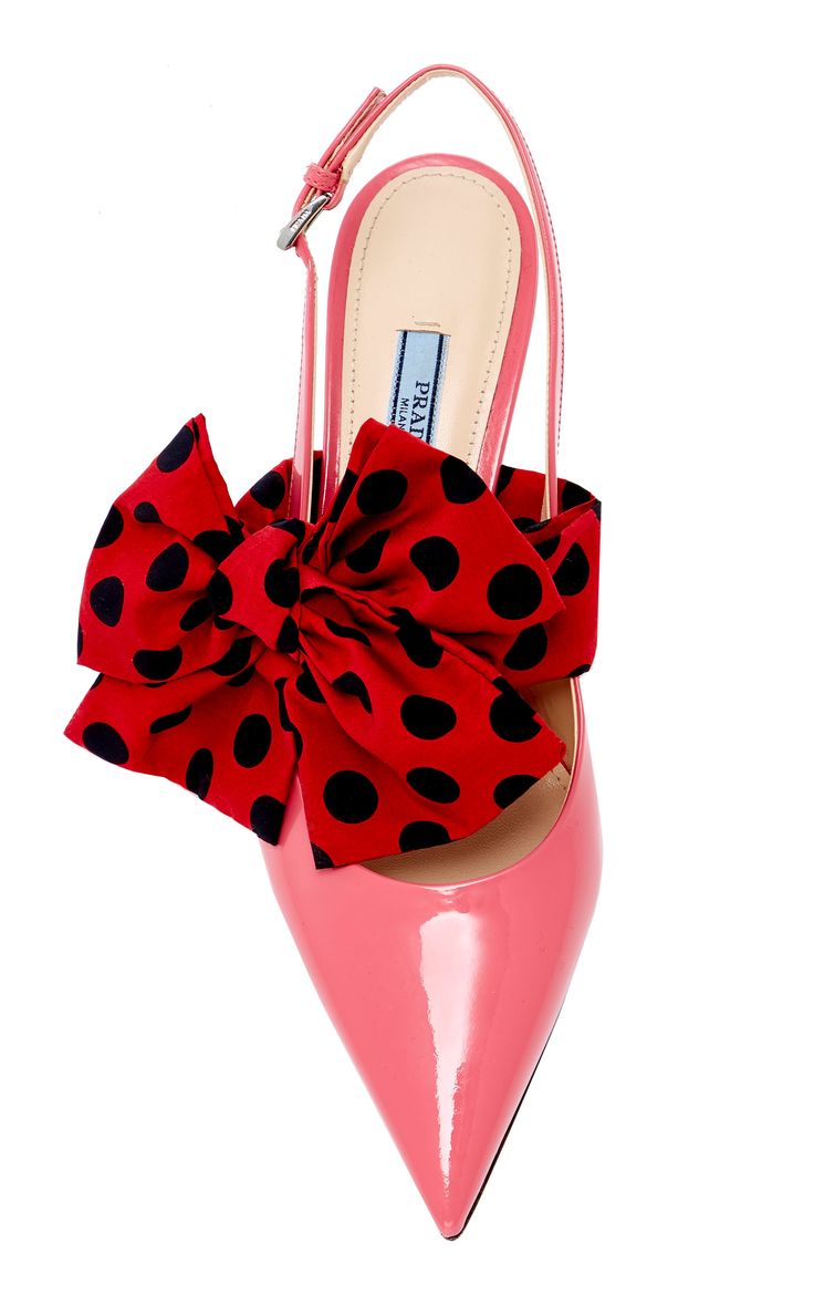 a closeup studio shot of a pink patent leather prada slingback heel with a large red polka dot bow.