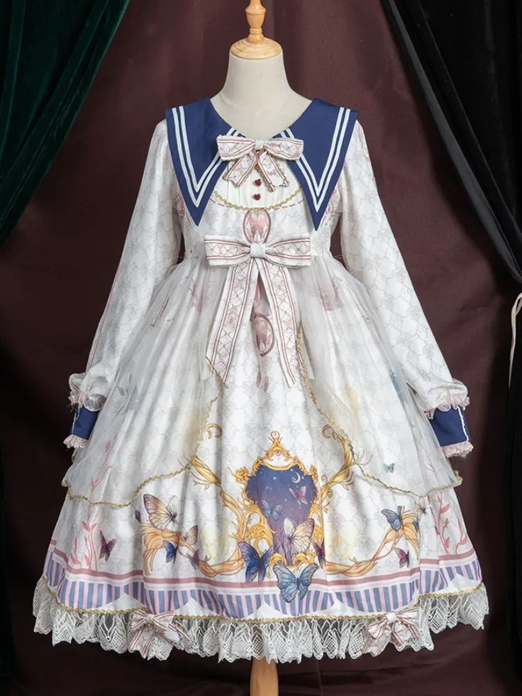 a white lolita fashion dress with a blue sailor collar is shown on a mannequin. the dress has long sleeves, a cinched waist, and a flowing skirt. the fabric features a pattern of butterflies, stars, and celestial motifs. the dress is adorned with lace trim and a large bow at the waist. the mannequin is positioned in front of a dark backdrop with velvet curtains. the lighting is soft and diffused, creating a romantic and ethereal atmosphere.