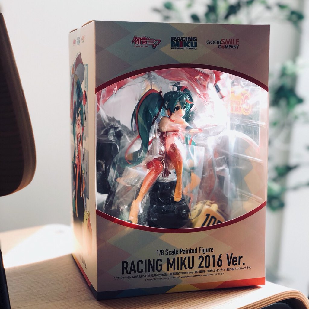 a photo of a  "racing miku 2016 ver." figure still in its box. the box features a window showing the figure of  "racing miku" inside. the box is sitting on a wooden surface.