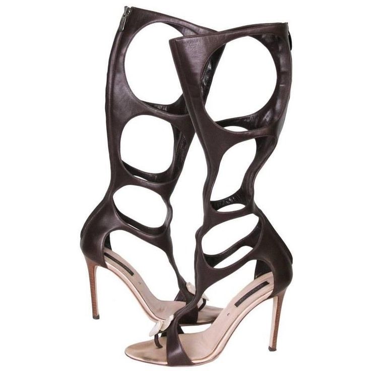 a pair of brown leather, cutout, gladiator sandals with stiletto heels are shown. the sandals are kneehigh and have a unique design with multiple circular cutouts. they appear to be made of highquality leather and have a sleek, elegant look. the shoes are positioned on a white background.