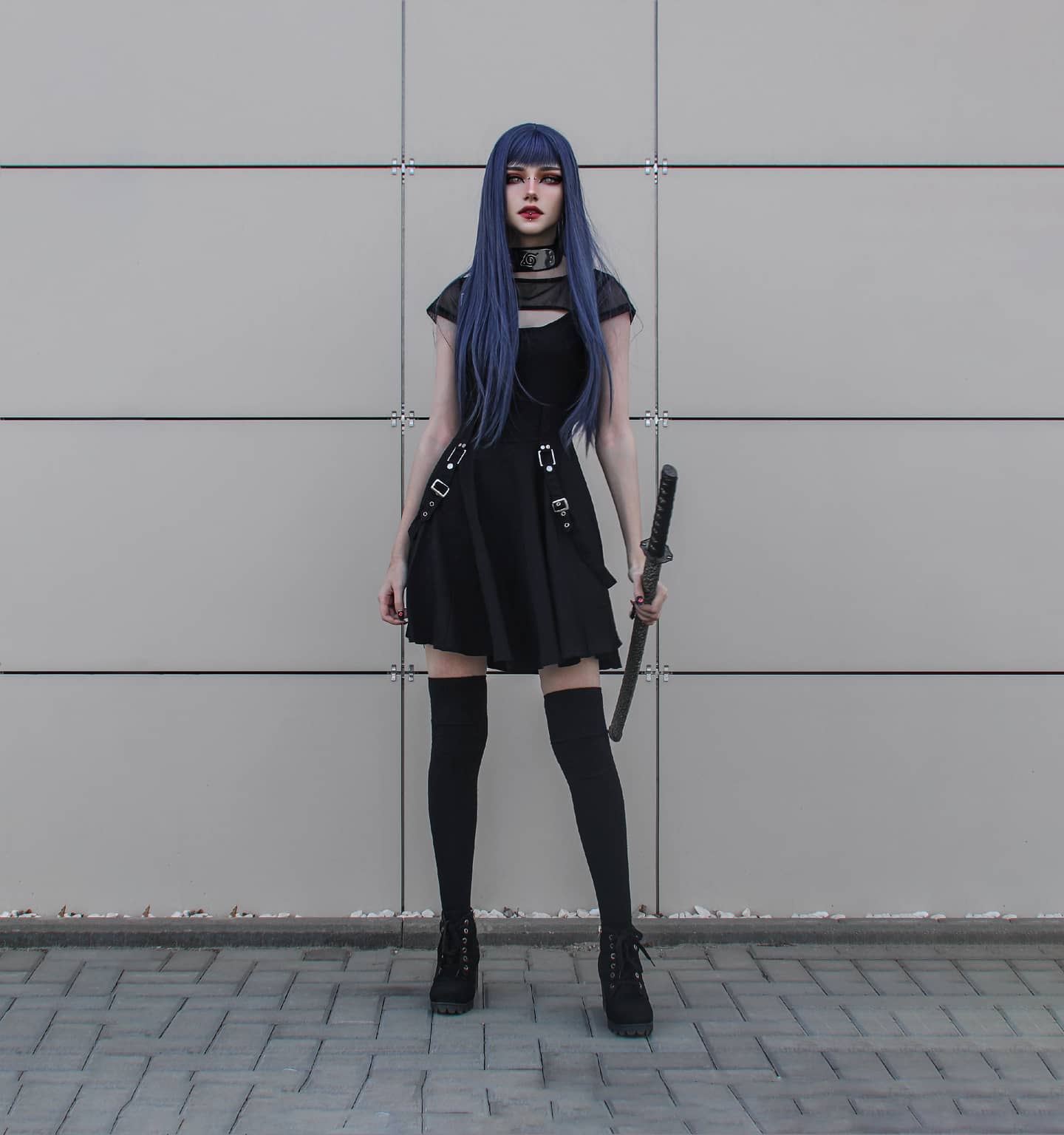 a full shot of a young woman cosplaying as an anime character. she's wearing a black gothic lolitastyle dress, black thighhigh stockings and boots, and has long, blue hair. she's holding a katana and standing against a grey wall outside.  the overall aesthetic is dark and edgy.