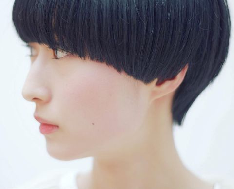 a young woman with short black hair and bangs looking at the camera. she has a neutral expression. her skin is clear. she is wearing a white shirt. the background is white. the lighting is bright and soft. the focus is on the woman's face.