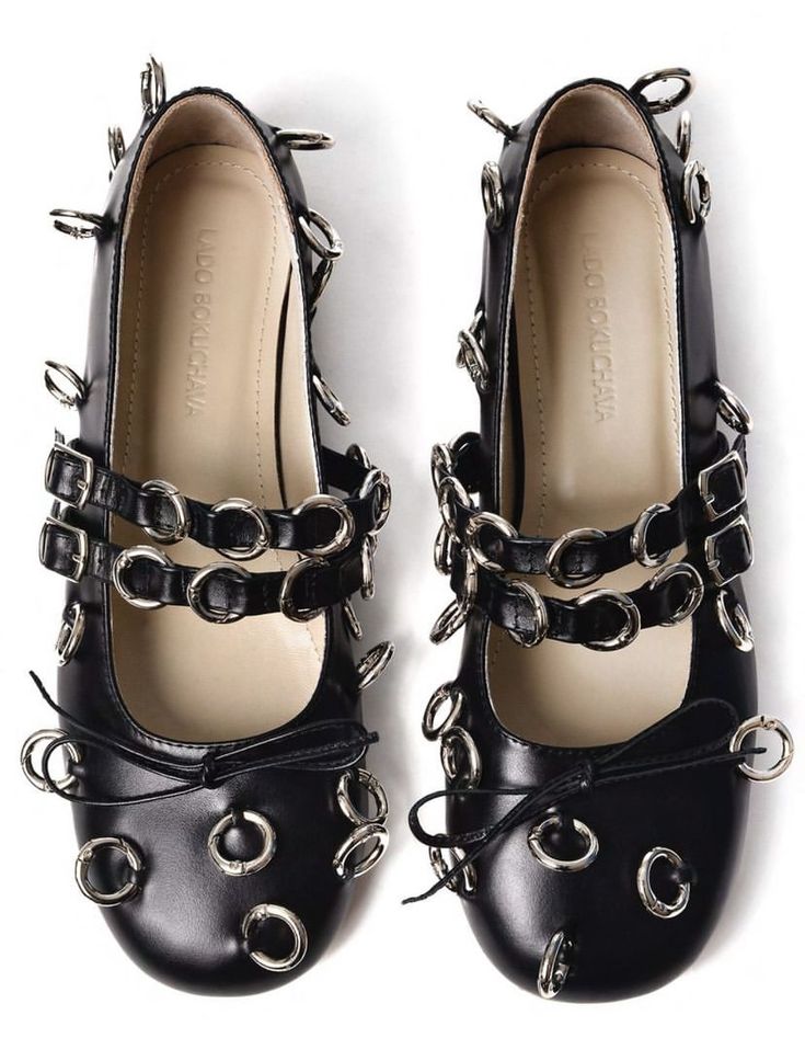 a closeup top view of a pair of black leather women's shoes.  the shoes are mary jane style flats with multiple straps adorned with silver metal rings and grommets. the brand "do bokuchwa" is visible inside each shoe. the shoes have a slightly pointed toe and a glossy finish. they appear to be stylish and possibly part of a designer collection.