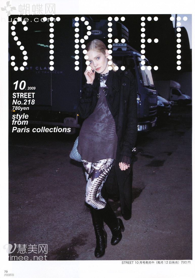a blonde woman in a long black coat, grey dress, patterned leggings, and black boots is posing on a city street at night. there is a truck in the background and japanese text on the left and right side of the image.  the image appears to be from a japanese fashion magazine.
