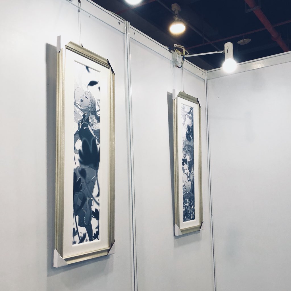 the image shows two pieces of black and white artwork hanging on white walls in an art gallery. the artwork is framed in goldcolored frames and depicts stylized characters. the lighting in the gallery is artificial.