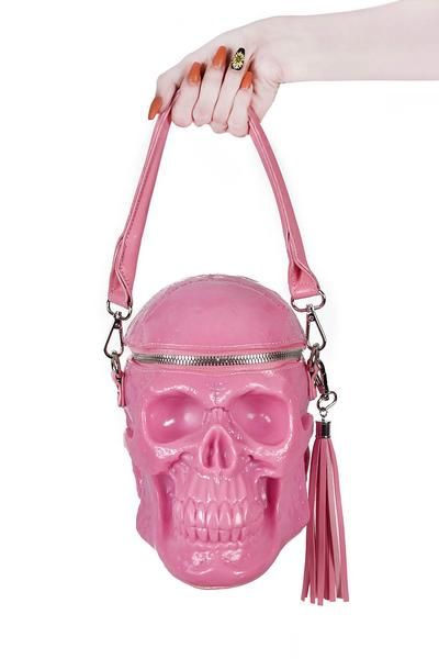 a hand holds a pink skullshaped handbag with a pink tassel. the hand has painted nails and a gold ring.