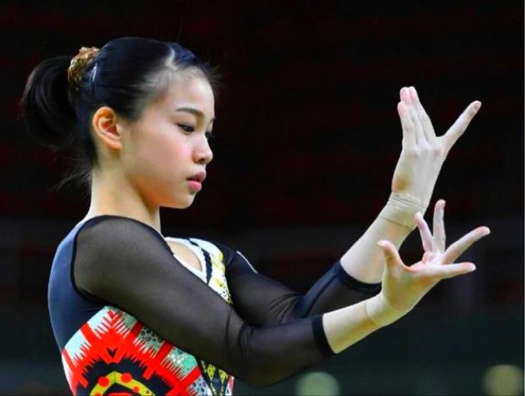 a young female gymnast in a black, red, and yellow leotard is shown midpose, her hands in a complex position, showcasing her flexibility and strength. her focus is intense as she completes a challenging exercise.