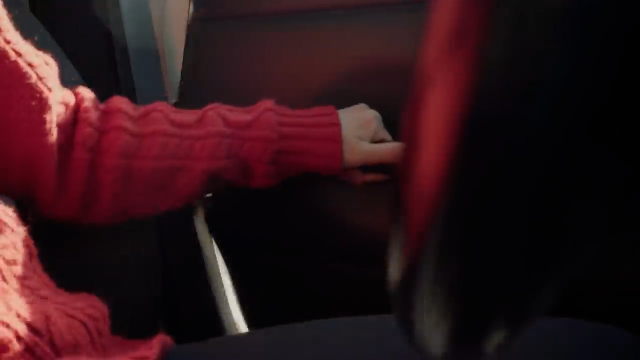 a closeup image of a person's arm and hand resting on a car door.  the person is wearing a textured, red sweater. the car's interior is dark, and sunlight streams through the window, casting shadows.