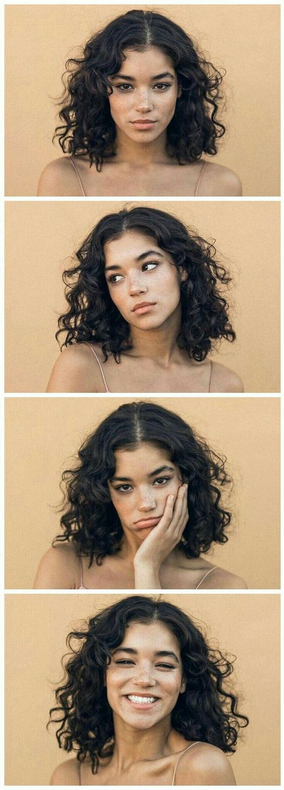 a young woman with long curly black hair looking directly at the camera. she is wearing a white background and is posing in a studio. she has a beautiful face and looks confident and happy.