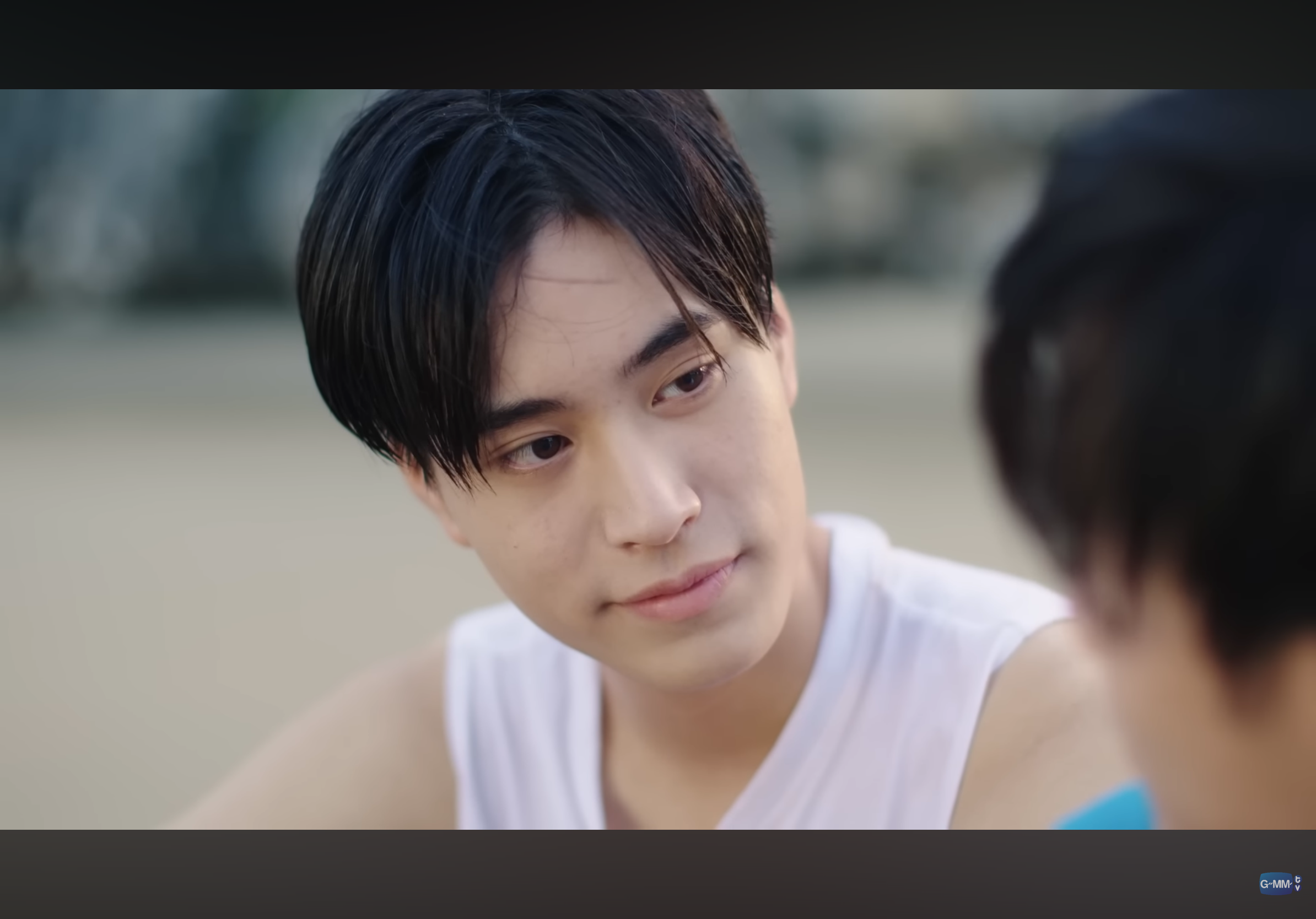 a closeup shot of a young man with dark hair and a gentle smile on his face. he is looking intently at someone offscreen, and the soft, natural lighting highlights the warmth in his expression. the setting appears to be a beach, with sand visible in the background, hinting at a relaxed and intimate atmosphere.  the overall mood suggests a romantic connection or a tender moment between two people.