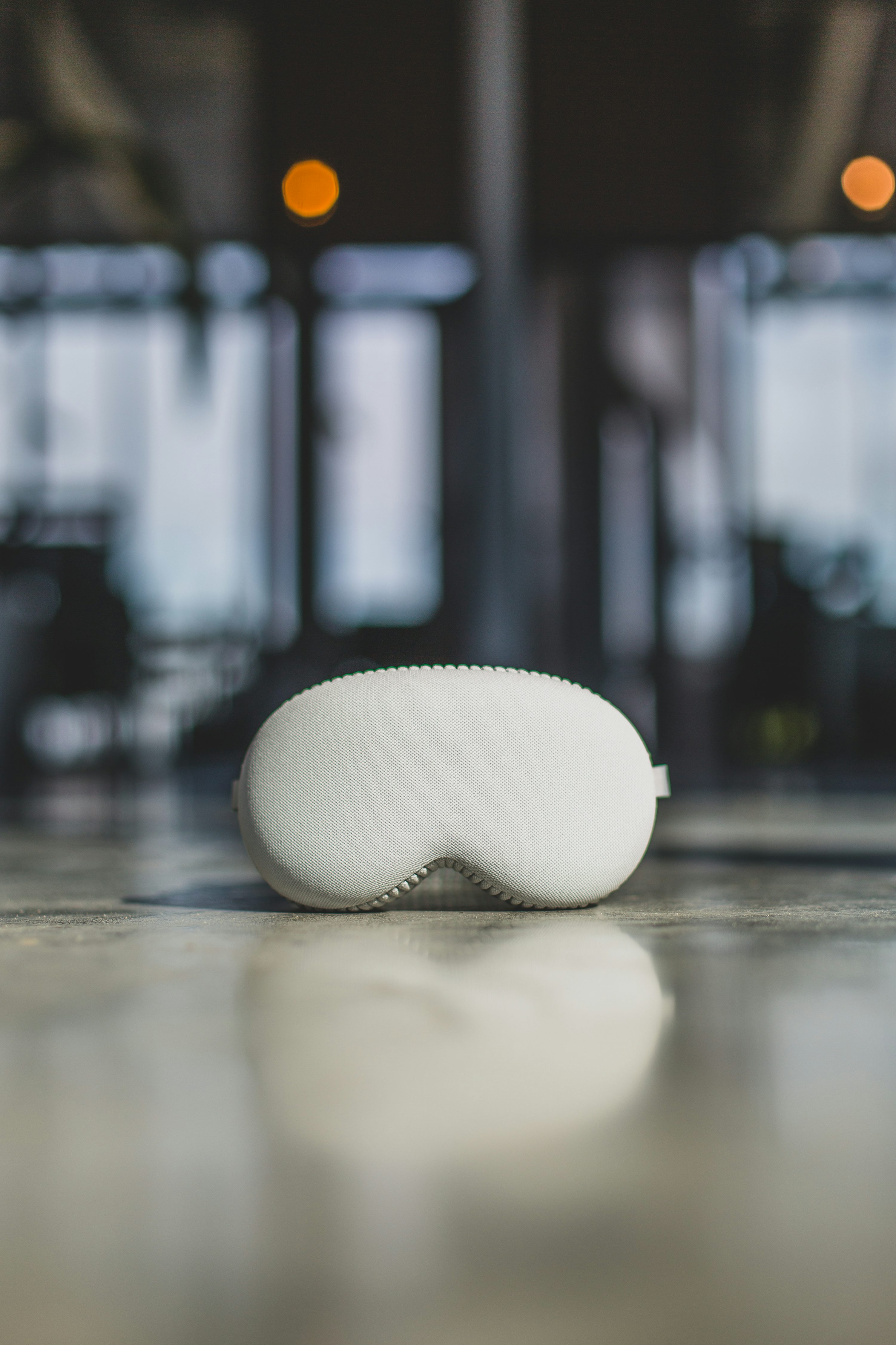 a white sleep mask sits on a shiny, reflective floor. in the background, there is a building or office space.