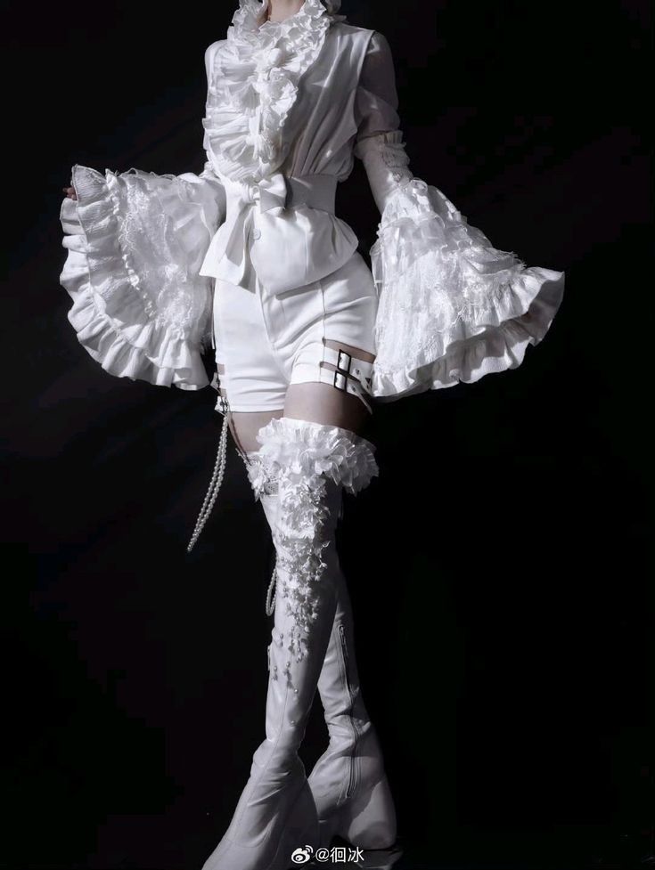 a person is wearing a highly stylized, allwhite outfit with victorian and fantasy elements. the outfit includes a ruffled top, shorts with a belted detail, and thighhigh boots adorned with lace and possibly pearls. the sleeves are long and flared with ruffled edges. the background is black.