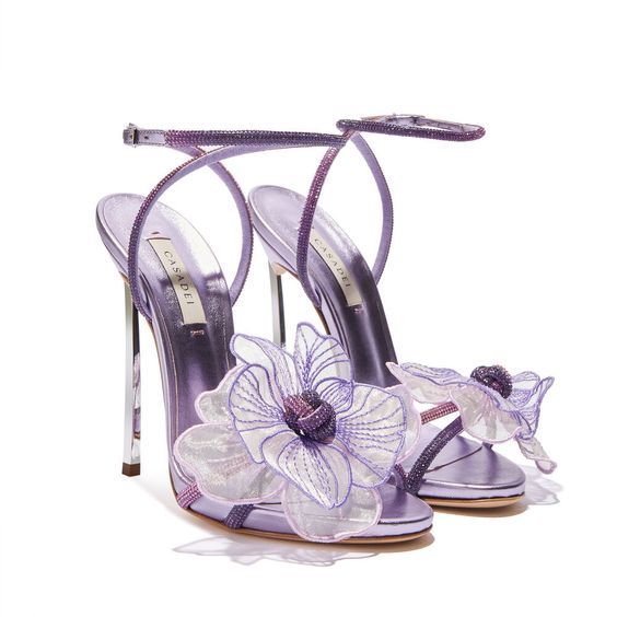 a pair of purple, floralembellished highheeled sandals with ankle straps are presented on a white surface. the sandals are designed with stiletto heels and feature delicate flower accents on the front. the "casadei" logo is visible on the insole of one shoe.