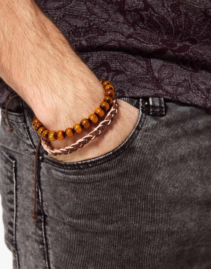 a closeup shot of a man's hand wearing a leather and wooden beaded bracelet. the man is wearing a dark gray tshirt with a floral pattern and jeans. the bracelet is on his left wrist. the image is focused on the bracelet and the man's hand.  it is a simple, relaxed, and casual look.