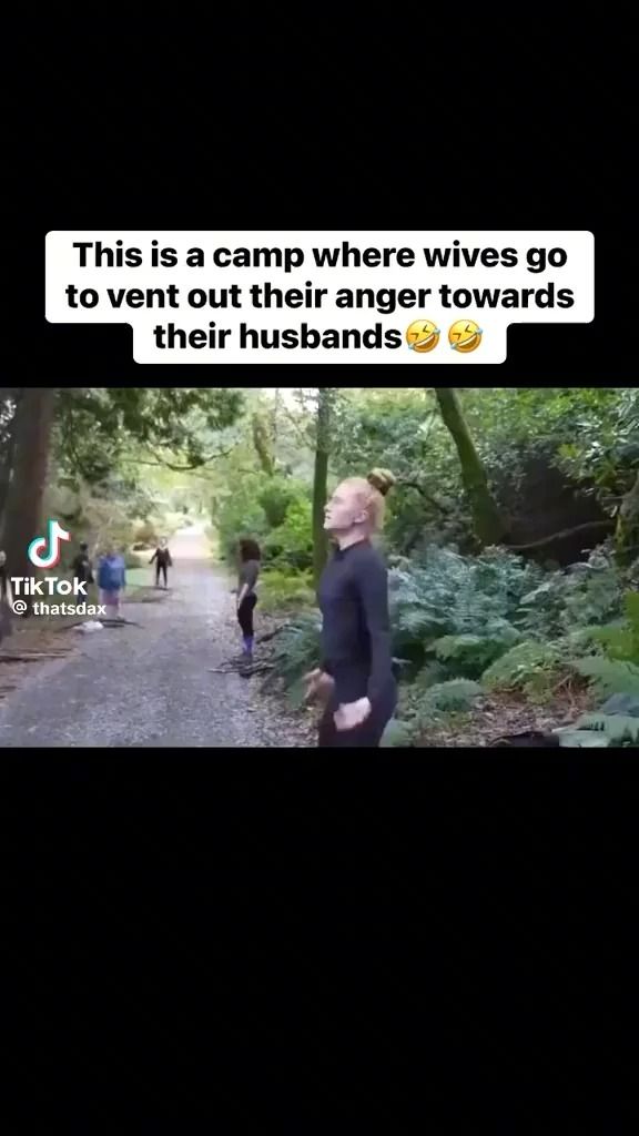 the image shows a tiktok video with the text "this is a camp where wives go to vent out their anger towards their husbands". the video depicts a path in a forest with women standing along the path.