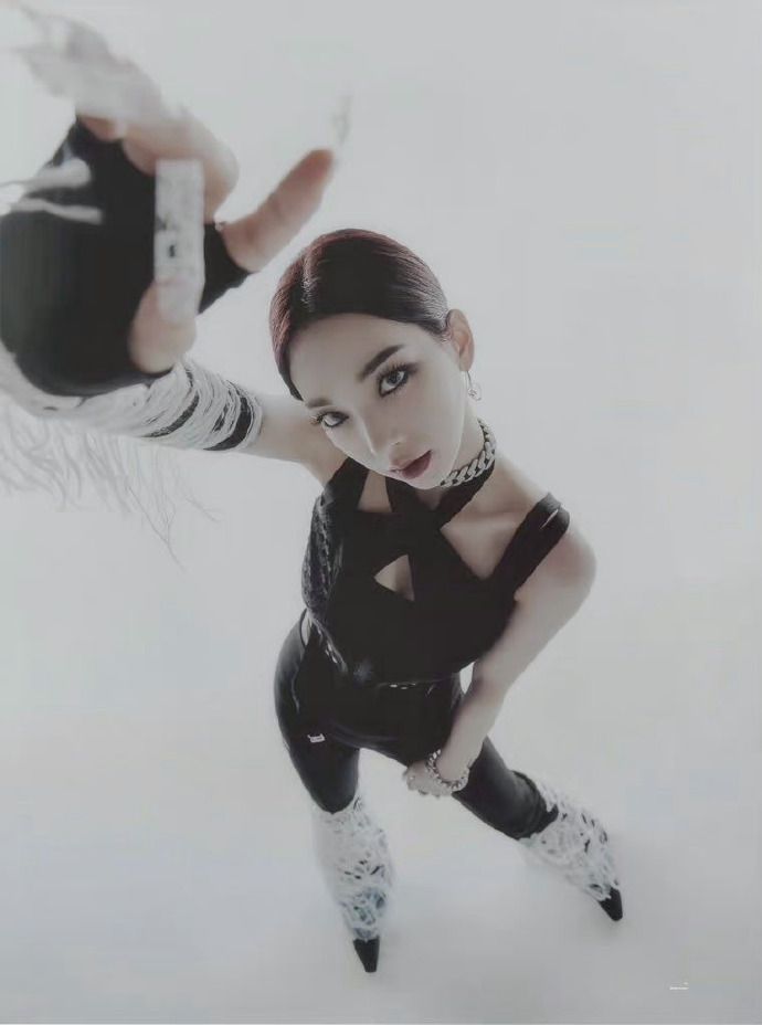 a woman in a black top and pants, white boots, and white gloves, is posing in a studio with a white background. she's looking directly at the camera, her gaze intense. her hair is pulled back and her makeup is dark and dramatic. she's giving off a fierce and confident vibe.