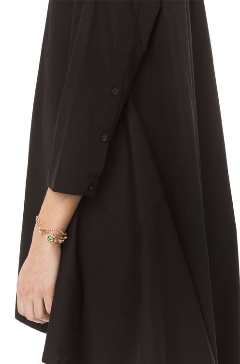the image shows a closeup of a person wearing a black dress and a gold bracelet with a green stone. the dress has long sleeves with buttons on the cuff.