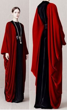 a woman wearing a long, red and black dress. the dress is made of velvet and has a capelike design. the woman is standing with her arms at her side, and she is looking at the camera. she is wearing a black dress underneath the red cloak. the dress has a high neck and is fitted. it is a simple but elegant design. the woman is wearing her hair down and has a natural makeup look. the dress has a black trim around the neck and wrists, and it flows down to her feet.