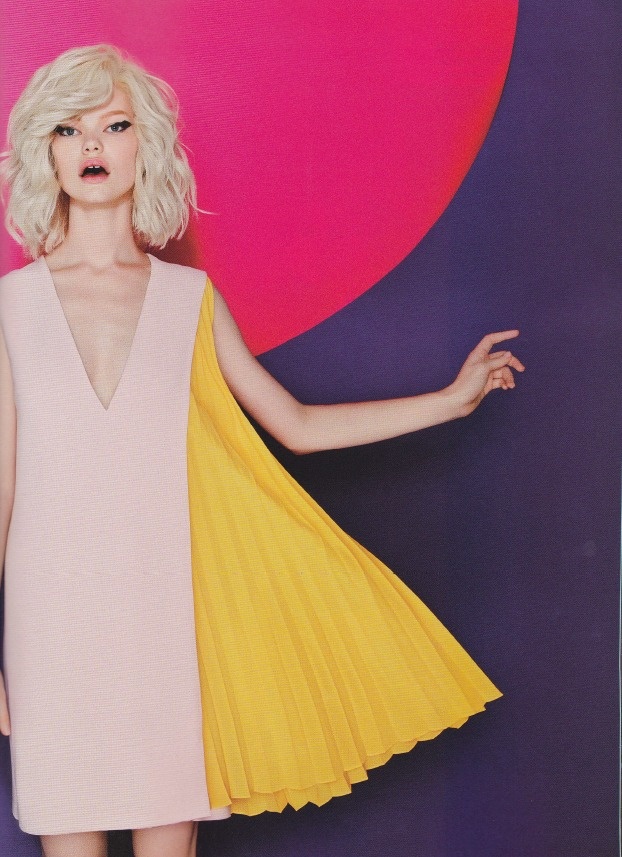 a woman with blonde wavy hair is wearing a pink sleeveless dress with a vneck and a pleated yellow fabric attached to the side. she has pale skin and her mouth is slightly open. the background is a vibrant mix of pink and purple. the image has a fashion editorial feel.