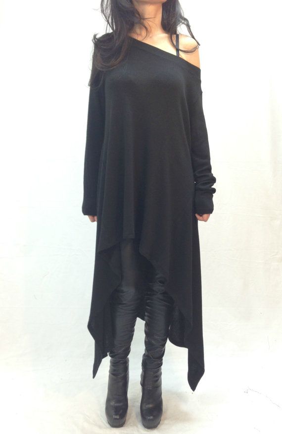 a woman is standing in front of a white background wearing a black offtheshoulder longsleeved dress over black leggings and black platform boots. the dress is asymmetrical with a longer length on one side.
