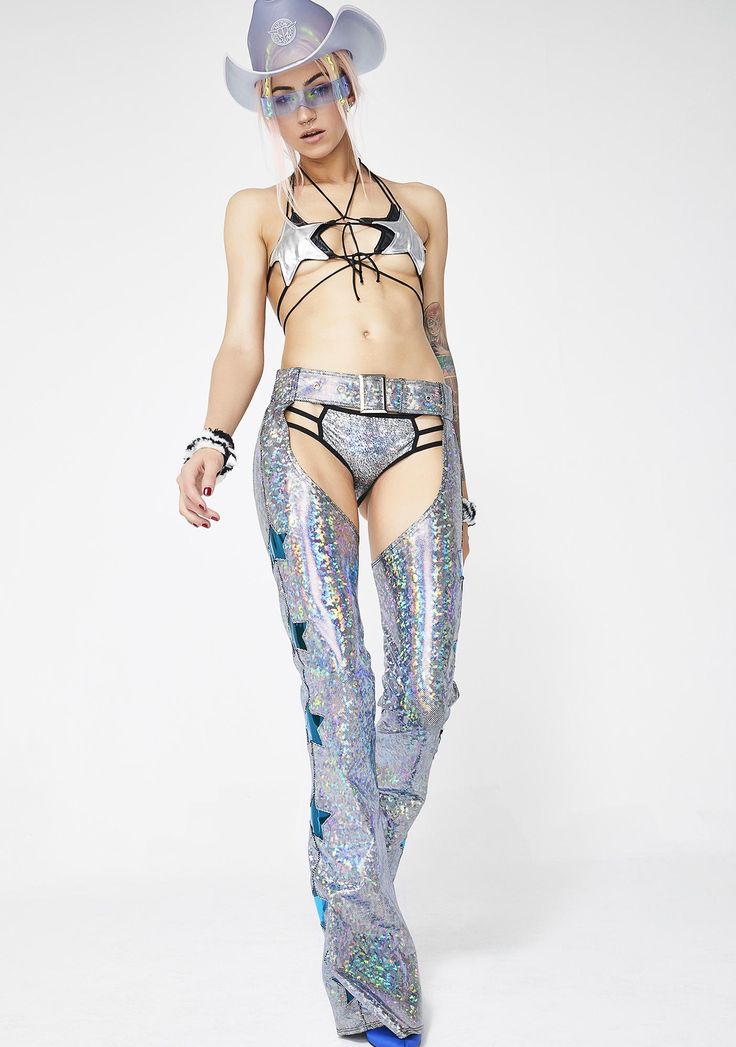 a woman wears a silver iridescent outfit with stars, a cowboy hat, and sunglasses, posing in a studio.