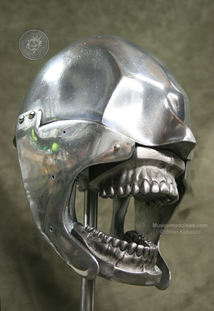 this is a closeup of a metal sculpture of a skull with an open mouth. the skull is made of polished metal and has a helmet on top. it is a unique and striking work of art, with intricate details and a realistic portrayal of human anatomy. the sculpture is likely on display in a museum of oddities.