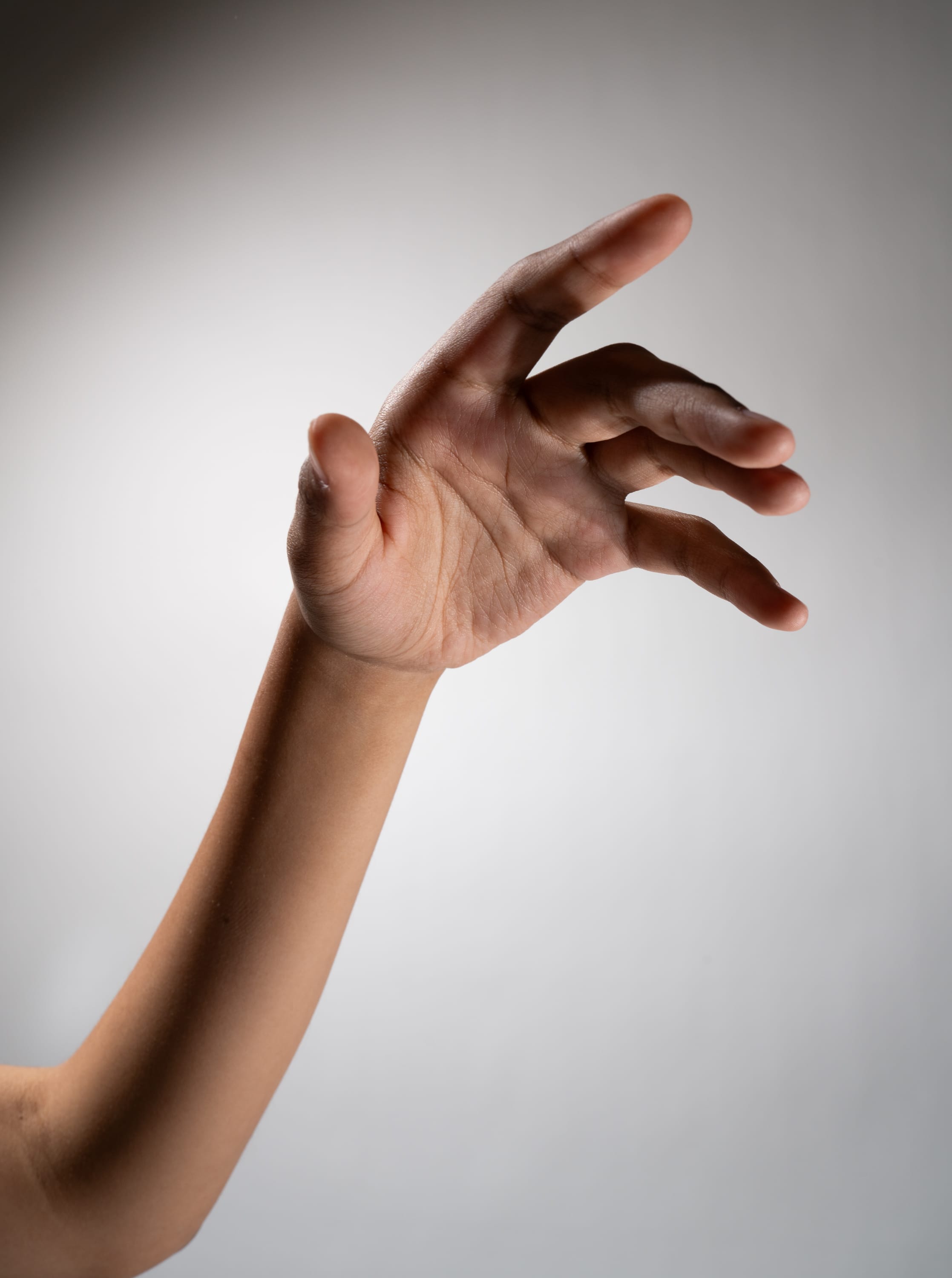 a closeup shot of a person's outstretched hand and arm against a plain gray background. the hand is reaching out, fingers spread open as if grasping for something. the studio lighting creates a subtle shadow, emphasizing the shape and texture of the hand.
