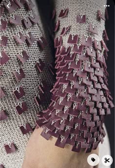 a close up shot of a clothing item, the fabric is made of a textured, gray and maroon material. the pattern is abstract, geometric and repeating. the piece has a handmade quality.