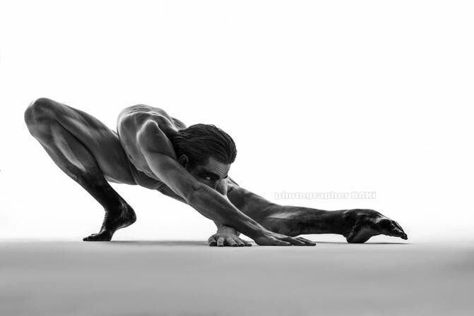 a black and white photo of a male contortionist stretching his body in a dynamic pose. the image is simple and clean, with only the model and his shadow visible against a white background. he appears to be extremely flexible and strong, demonstrating the power of human movement.