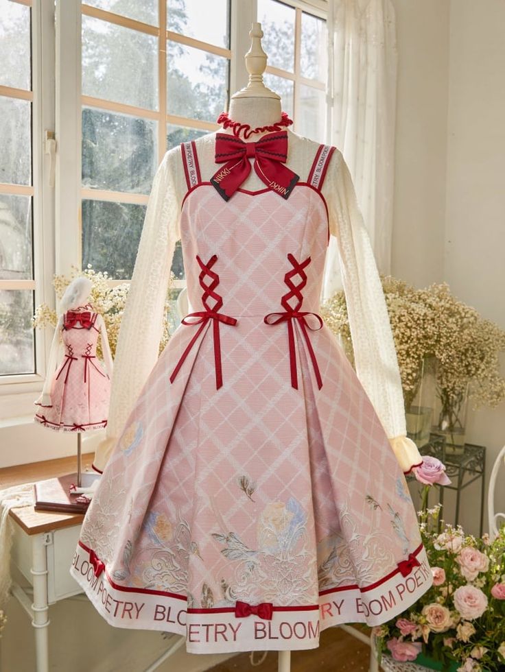 a pink lolita fashion dress with floral and ribbon details is displayed on a mannequin. the dress is shown in a welllit room with a window in the background. the scene also includes a smaller doll wearing a matching outfit and a table with flowers.