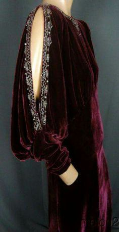 a woman is wearing a maroon velvet dress with silver embroidery. she is standing with her back to the camera. the dress is long and has a fitted bodice and a flowing skirt. the embroidery is on the sleeves and around the neckline. the woman looks elegant and sophisticated in this dress.