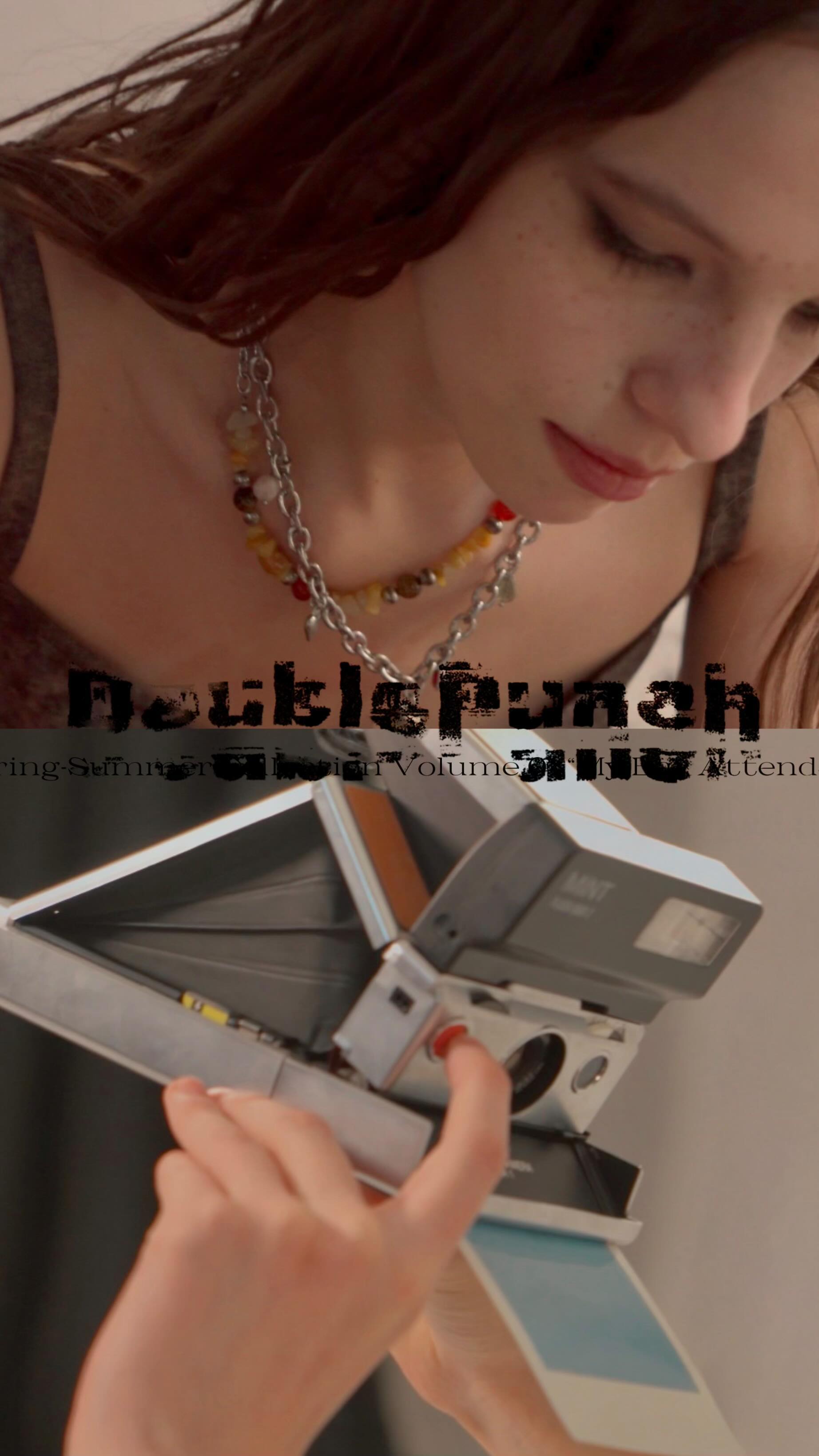 the image is a closeup, stylized portrait of a young woman with long, wavy brown hair. she's wearing a simple gray top and a layered necklace featuring both a beaded and a chain component.  her gaze is directed downward, seemingly focused on an old polaroid camera she holds. the camera is positioned prominently in the frame,  and a partially exposed photograph is visible. the overall aesthetic is evocative of vintage photography and 90s fashion.  text overlayed on the image appears to be a title or album art text, reading "double pumah". the mood is somewhat introspective and mysterious.
