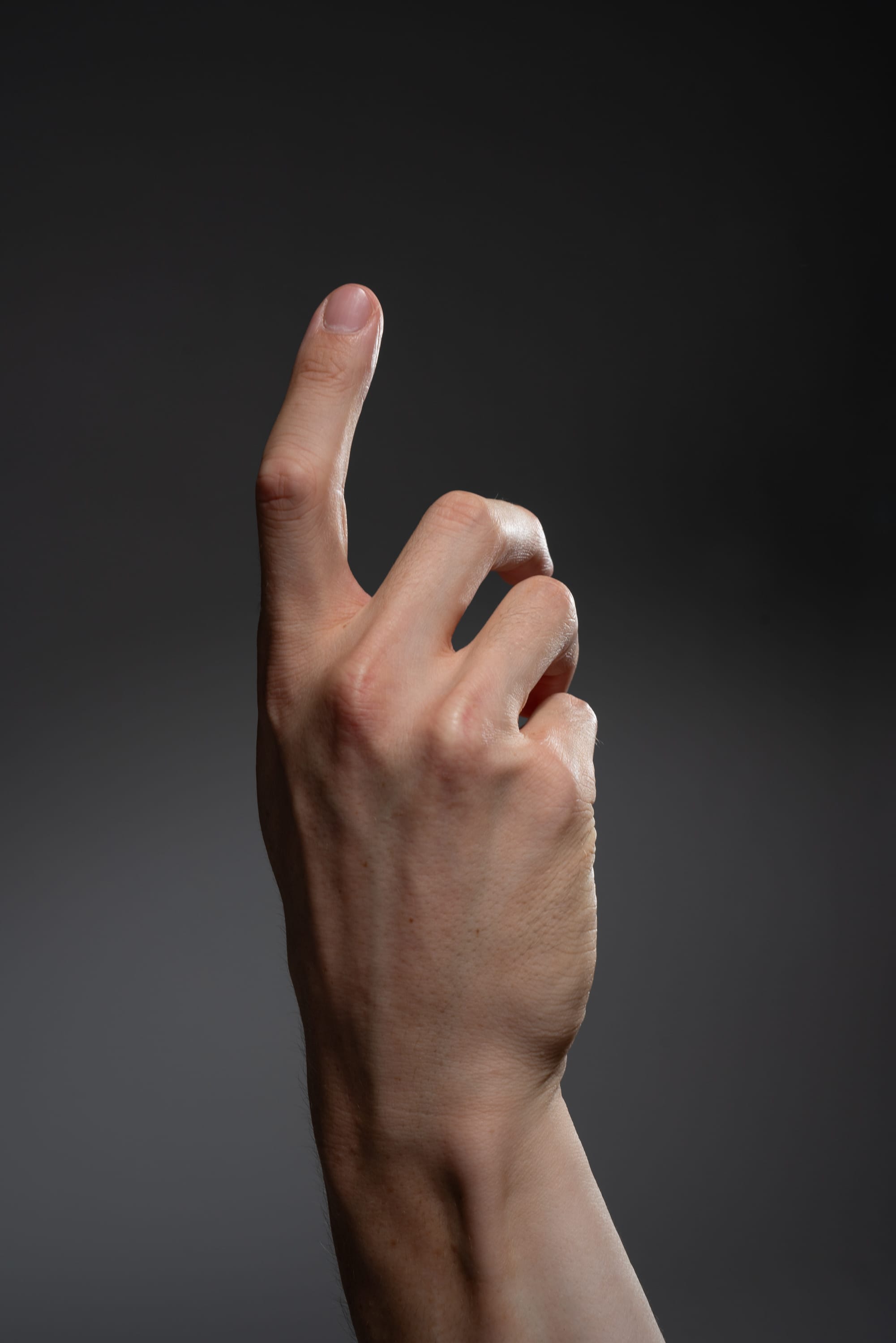 a hand is pointing upwards with the index finger extended against a gray background.