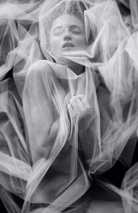 a black and white portrait of a woman with long hair, wearing a veil. the woman is shrouded in fabric, and her face is partially obscured. the image has a dreamy, ethereal quality, and the woman's expression is both mysterious and alluring. the fabric is soft and delicate, adding to the overall sense of beauty and romance.