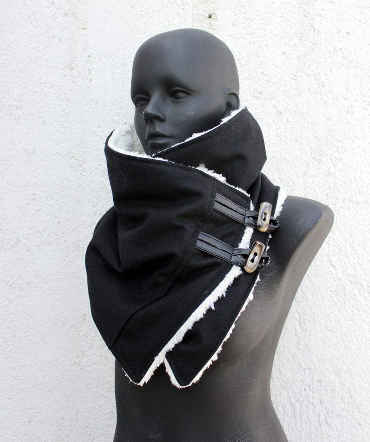 a black and white fur collar with buckles on a mannequin. the collar is made of a black fabric with a white fur lining. the collar is fastened with two buckles. the collar is displayed on a mannequin.