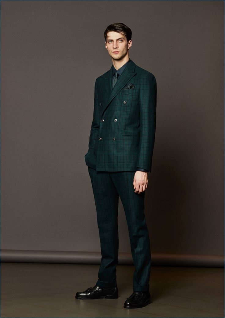 a fulllength studio shot of a man wearing a green plaid doublebreasted suit with matching pants, a green shirt, and a green tie. he is also wearing black dress shoes and has a pocket square in his jacket. the background is a neutral gray.