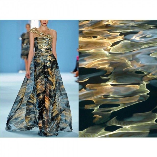 a model in a sheer dress with gold embellishments walks the runway at a fashion show. the dress is reminiscent of water, with its ripples and reflections. the fabric shimmers and catches the light, creating a beautiful effect.
