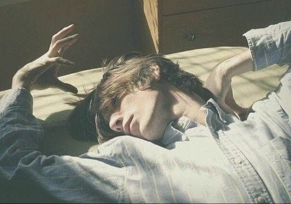 a man is lying down in a shirt. one hand is raised and there are shadows falling across him.