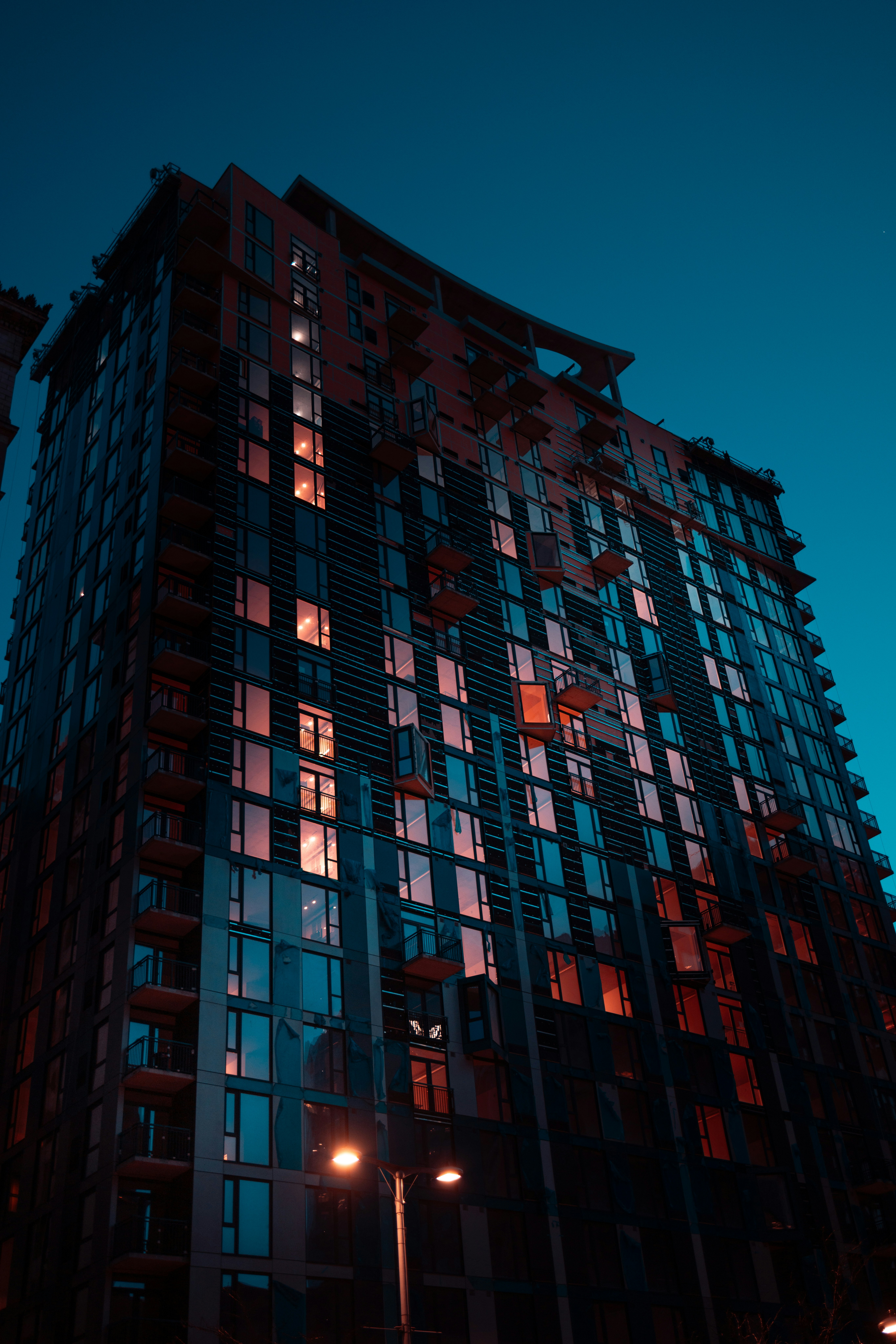 the image captures a modern highrise apartment building from a low angle perspective. the photo was taken at night, with the building illuminated by both interior and exterior lighting. the warm glow from the apartment windows contrasts with the cool blue tones of the night sky, creating a visually striking image.