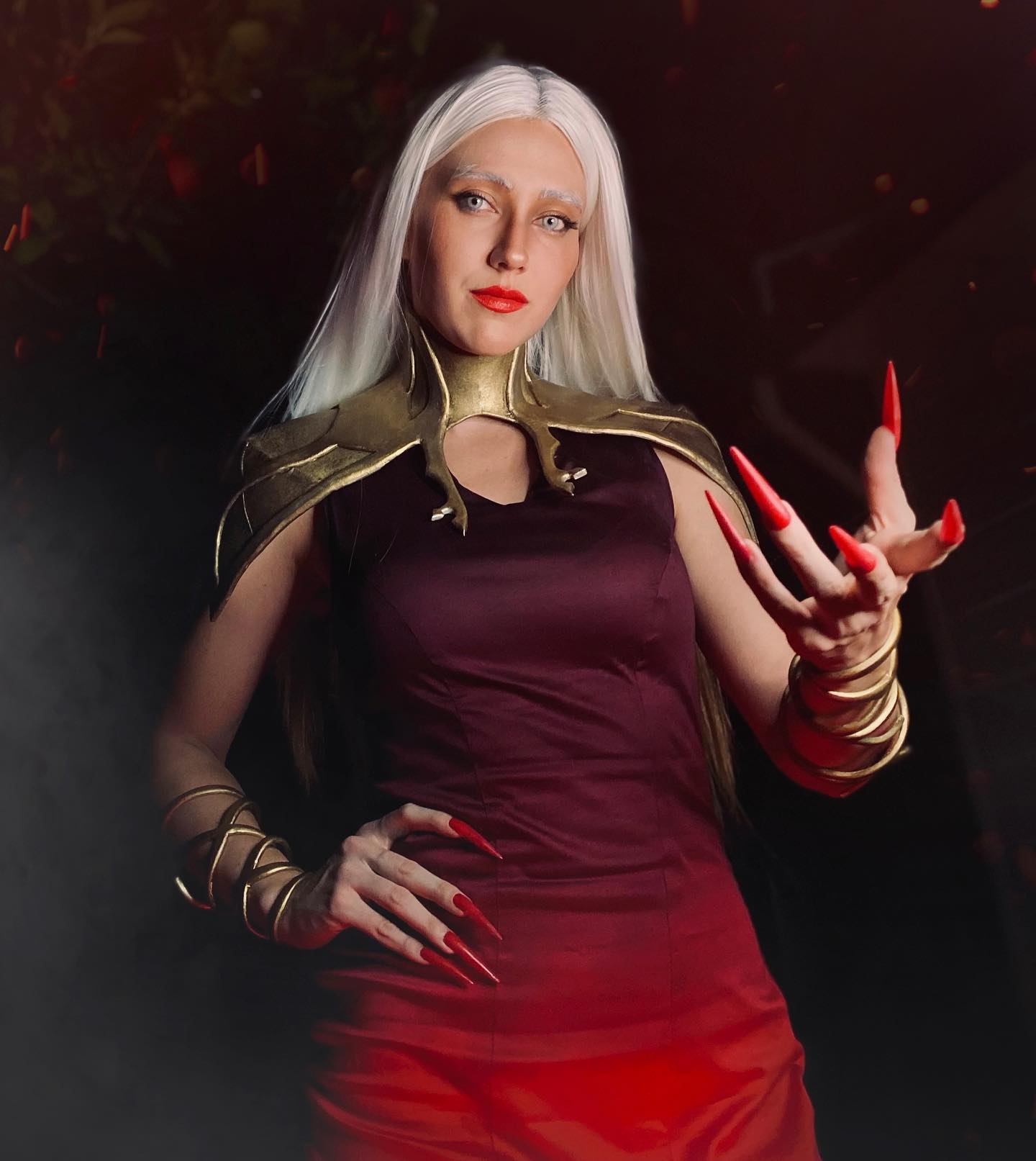 captivating cosplay photograph depicts a woman dressed as a sorceress.  she boasts long, flowing white hair, a dark red dress with a gold collar and shoulder pieces, and striking red nails. she holds one hand up, fingers extended as if casting a spell. the background is dark and moody, with hints of red light accentuating the overall dramatic effect. her expression is serious and powerful, enhancing the magical and mystical atmosphere of the image. the detail in the costume and the overall composition suggest a high level of artistic skill and attention to detail.