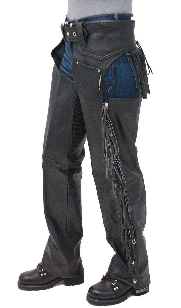 a full shot of a woman wearing black leather chaps with fringe detailing.  the chaps are worn over blue jeans, and she is also wearing black boots.  the image shows the chaps from the side, highlighting their style and fit.