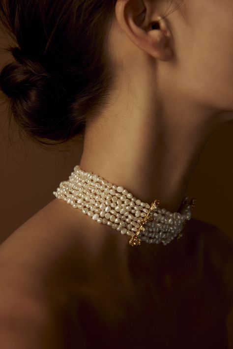 a closeup, softlylit portrait of a woman wearing a multistrand pearl choker with a gold clasp. the focus is on the necklace and the woman's elegant neckline, with her hair styled in a simple bun. the image exudes a sense of timeless beauty and sophistication.
