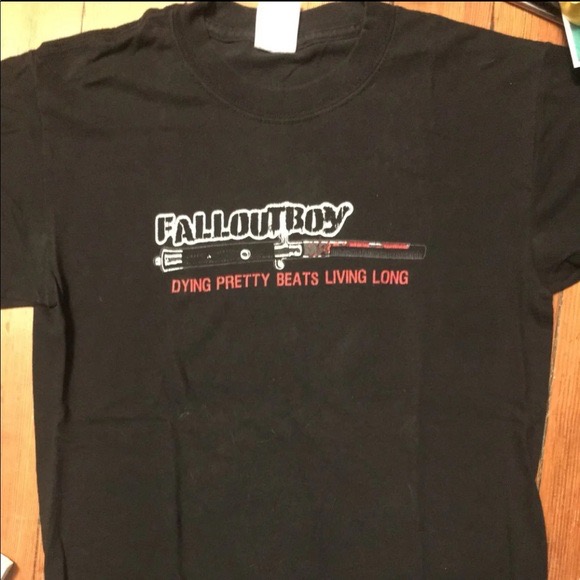 a black tshirt with the fall out boy logo printed on the front. the logo includes the band's name in white, with a red and white knife design underneath. the shirt has a red inscription that says "dying pretty beats living long". the shirt looks to be vintage.