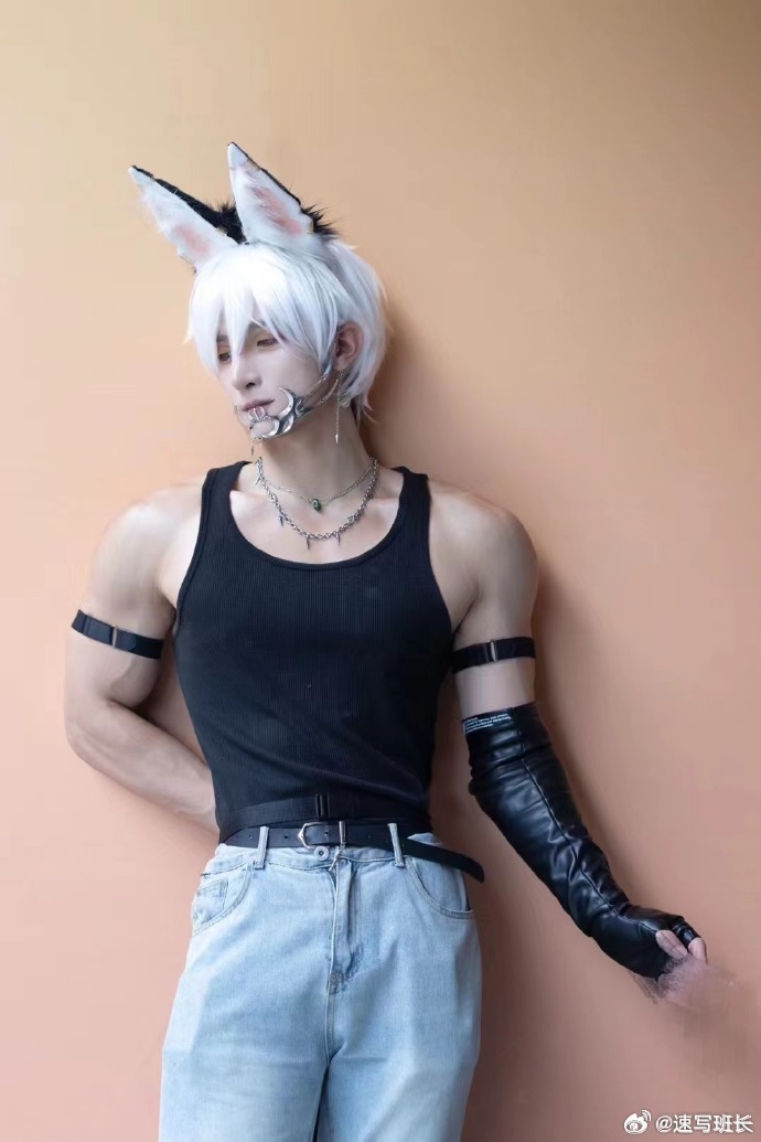 a man is dressed in cosplay attire. he is wearing a black tank top, light wash jeans, and black gloves. his hair is white and he has on a pair of rabbit ears. the background is a peach color.