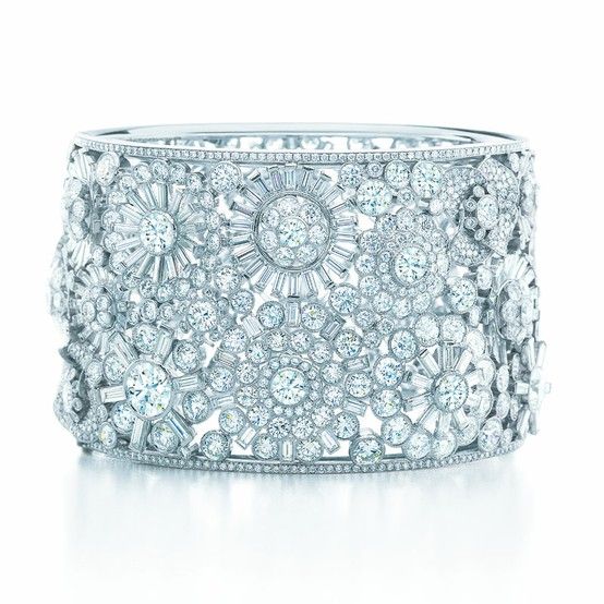 the image showcases a luxurious tiffany & co. diamond bracelet.  the bracelet is a wide cuff design, intricately crafted with a multitude of diamonds set in platinum. the diamonds are arranged in various shapes and sizes, forming a floral pattern of round and baguettecut stones.  the overall effect is a dazzling display of sparkle and brilliance, emphasizing the highend quality and craftsmanship of the piece. the bracelet is presented against a clean white background, allowing the jewelry to be the central focus.