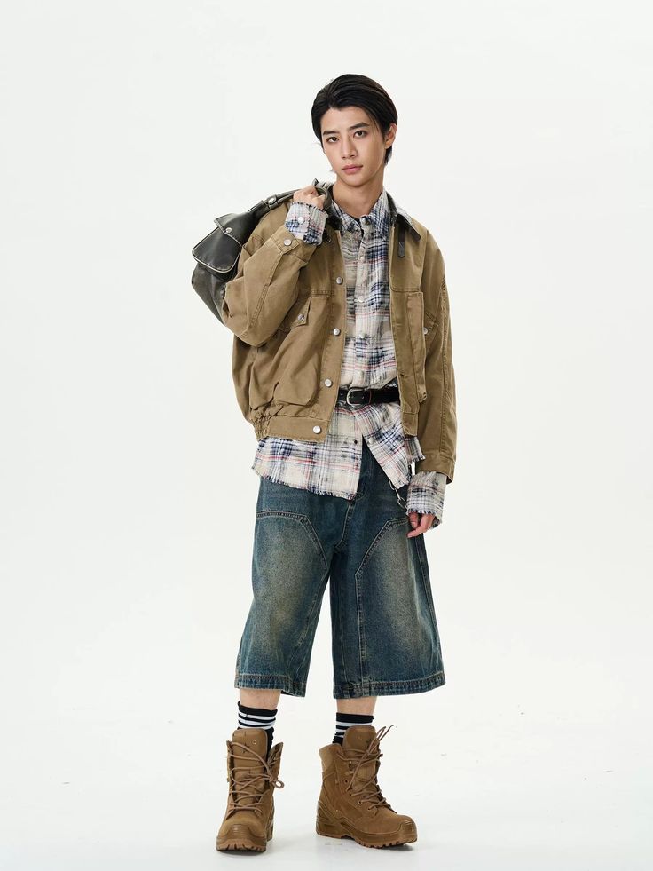 a young asian man is standing against a white background, modeling a casual outfit. he is wearing a tan work jacket over a plaid shirt, denim shorts, and brown work boots. he carries a brown leather bag over his shoulder.  his pose is relaxed yet stylish, showcasing the clothing and accessories. the image is welllit and professionally shot.