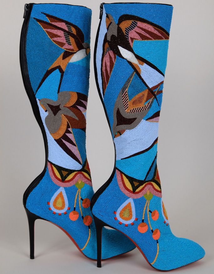 two turquoise, kneehigh, highheeled boots with intricate beadwork designs of birds and other patterns are positioned side by side on a neutral background. the red soles of the boots are visible, and the boots are designed with artistic flair, making them a statement fashion piece.