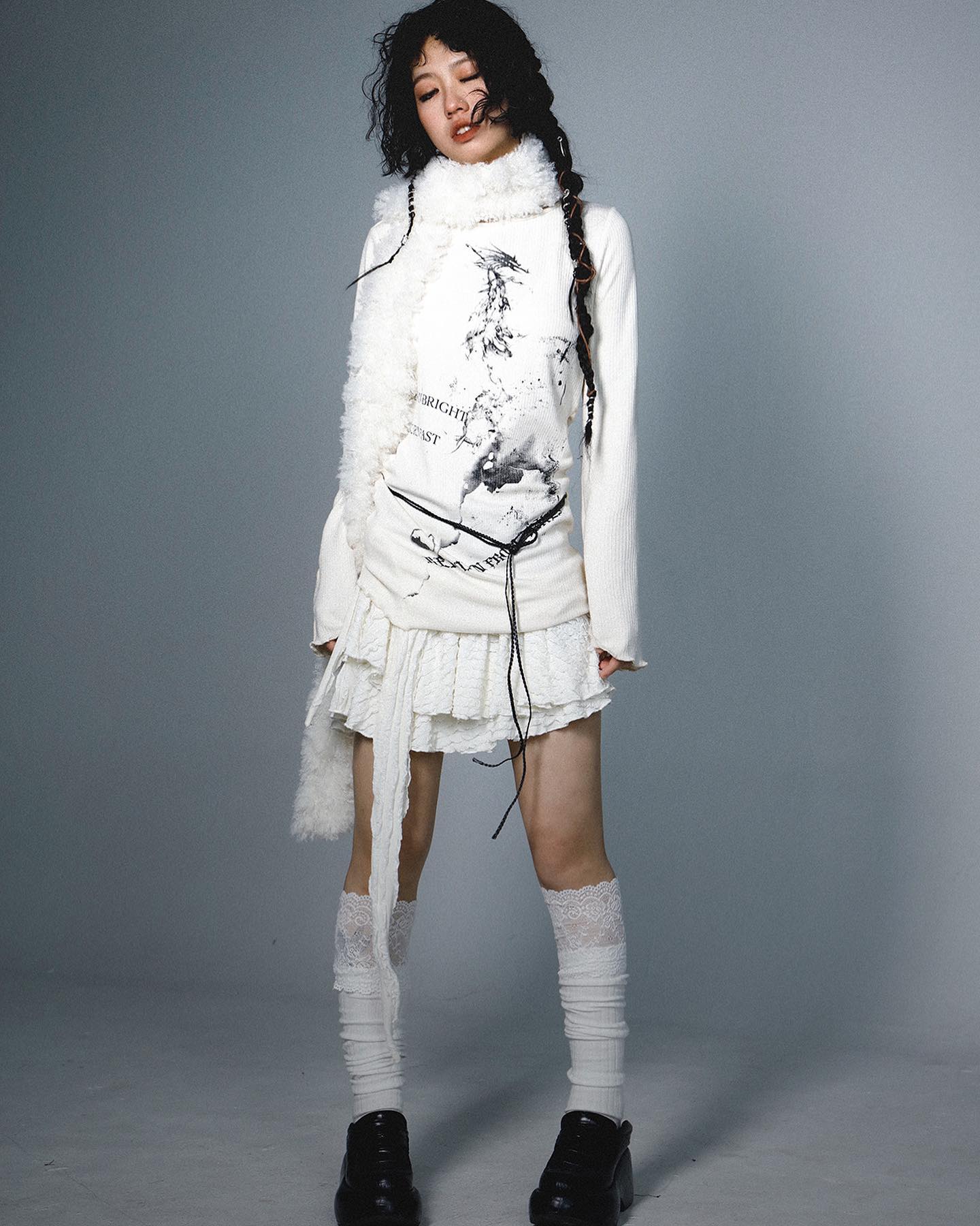 a full shot of a young asian woman showcasing a stylish white outfit. the outfit consists of a longsleeved turtleneck sweater with a unique print, a layered white lace skirt, long white socks with lace trim, and black ankle boots. the model is wearing a fluffy white scarf draped around her neck. her hair is styled with loose curls, and she has a slightly serious expression. the backdrop is a simple light gray studio setting. the overall style is elegant and chic, blending a touch of artistic and modern elements.